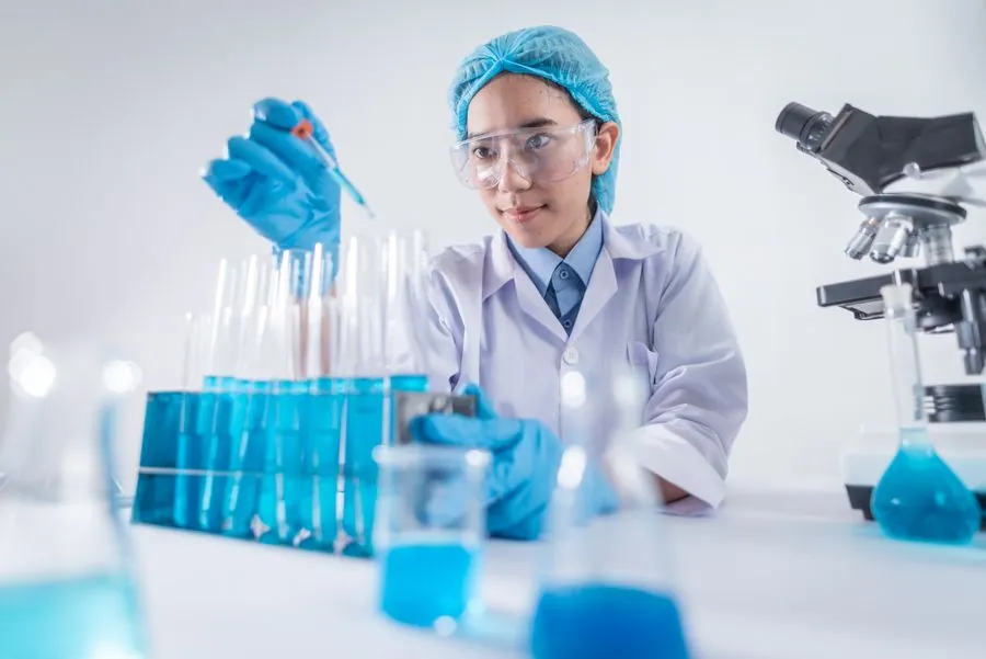 Mãos com luvas pesando e misturando insumos em vidraria de laboratório