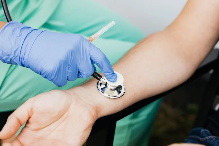 Profissional de luvas realizando um curativo no braço de um paciente sentado