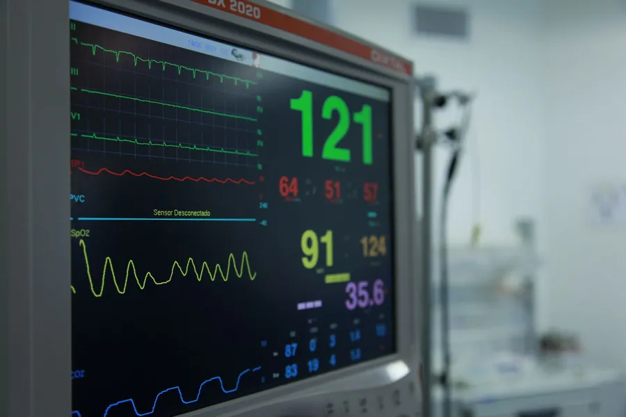 Tela de monitor multiparamétrico exibindo curvas e números de sinais vitais